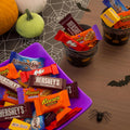 Assortiment Reese's, KitKat, Hershey's en Milk Duds in een paarse kom en zwarte emmers.