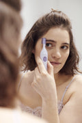 Vrouw gebruikt een paars-witte gezichtshaartrimmer bij haar wenkbrauwen.